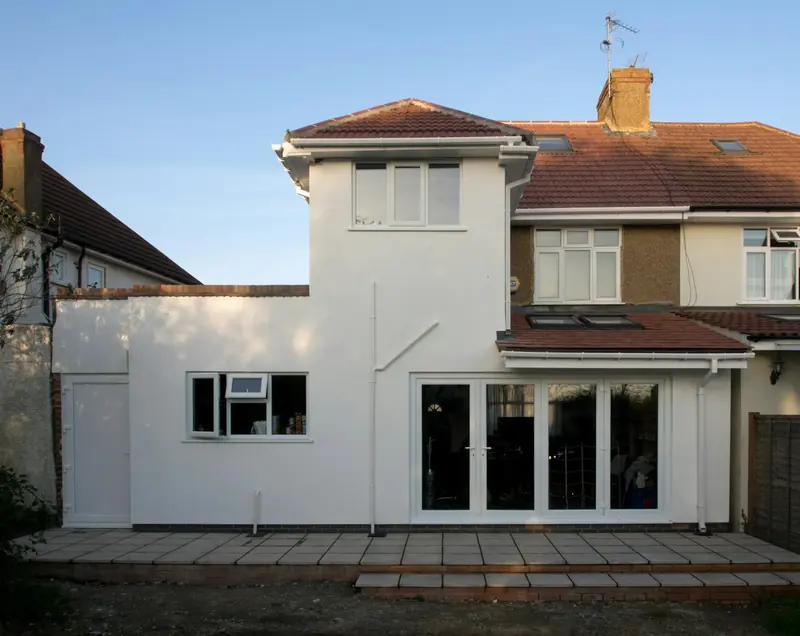 The rear of a 1930s semi-detached house with a white rendered two-storey extension and wide glazed doors