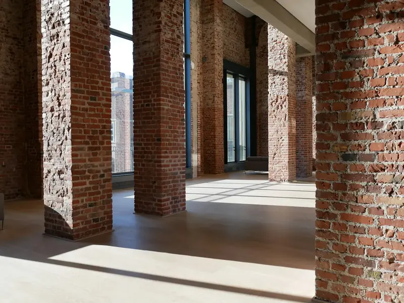 An empty room with brick piers, a pale timber floor and tall windows