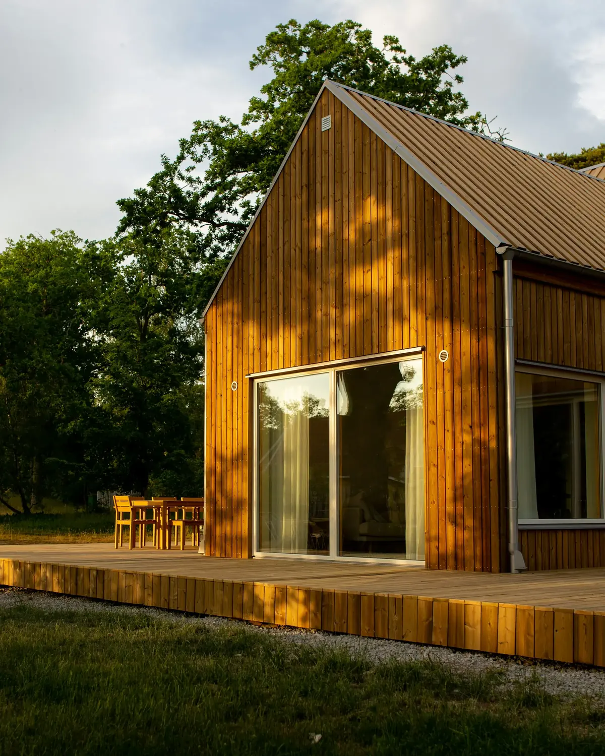 A gabled house clad in vertical larch boards, with a full-height glazed opening onto a timber deck