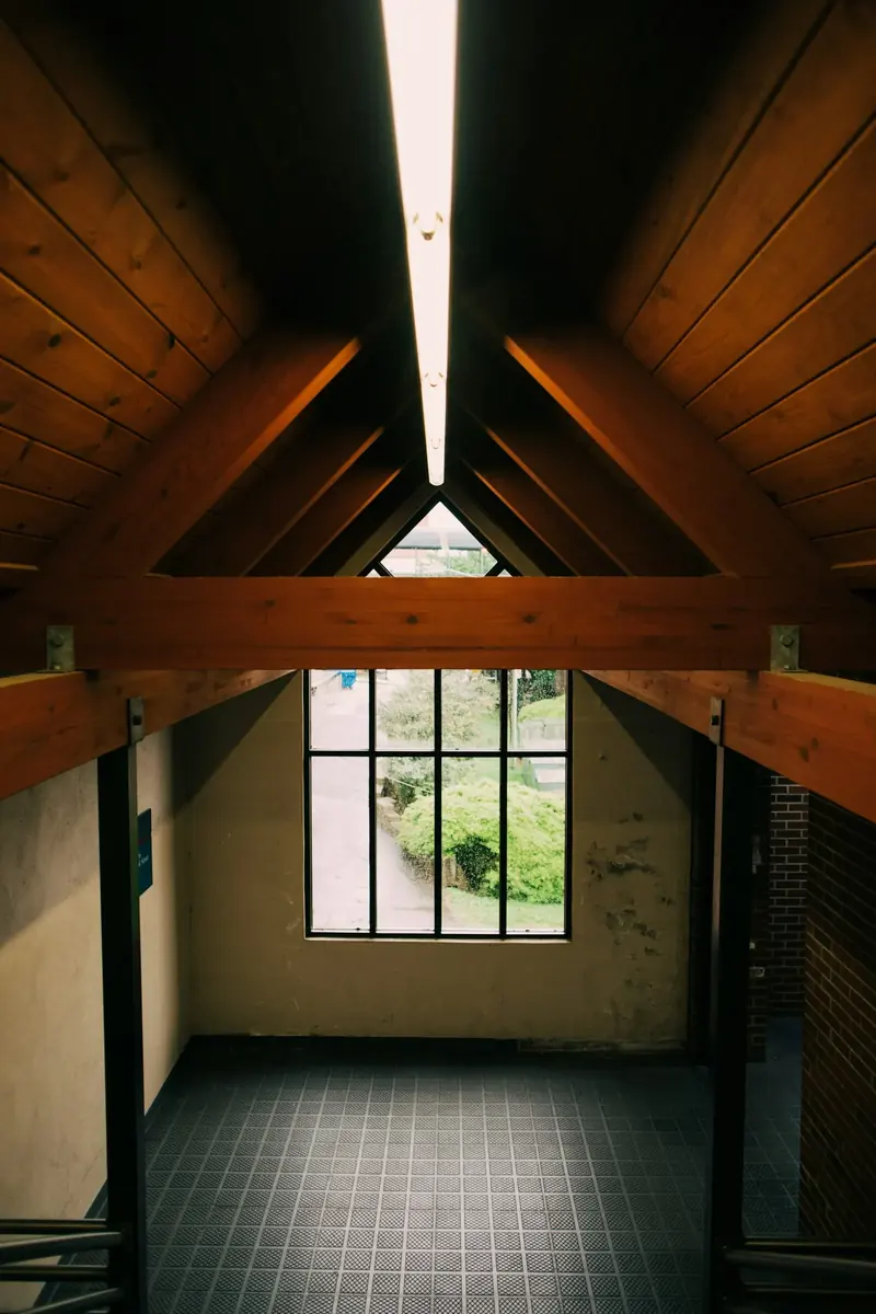 A tall window at the end of a room with an exposed timber roof