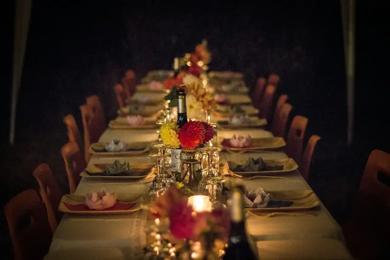 A long dinner table set with candles and flowers in a dark room