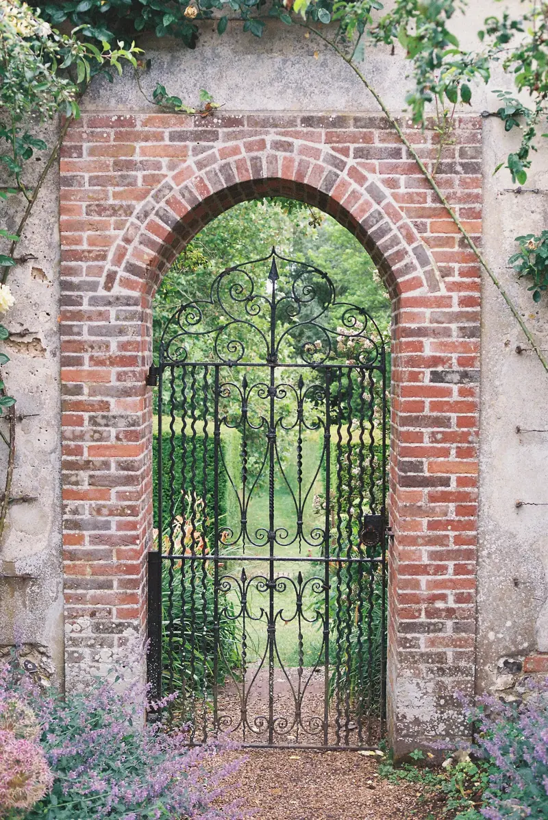 An iron gate set in a brick arch, with the walled garden beyond