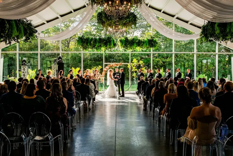 Guests seated in rows inside a glasshouse, facing a couple at the front