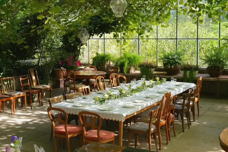 Long tables laid for dinner inside the glass Orangery, with greenery overhead