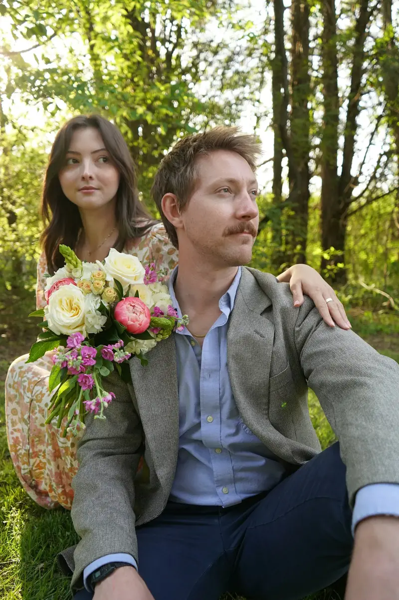 Couple sitting in a wood, one holding a bunch of garden roses