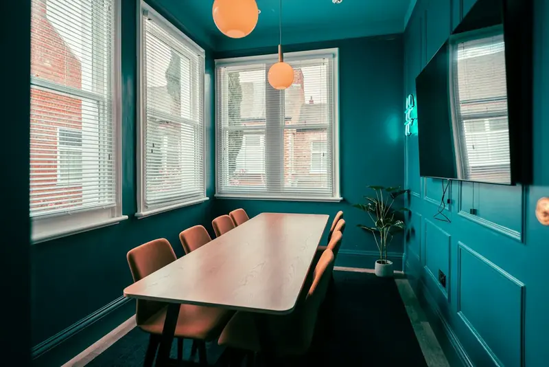 A small meeting room with a long table, teal walls and tall sash windows